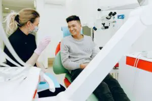 https://www.pexels.com/photo/man-sitting-on-dental-chair-3845810/ Man sitting in dentist’s chair speaking with dentist.